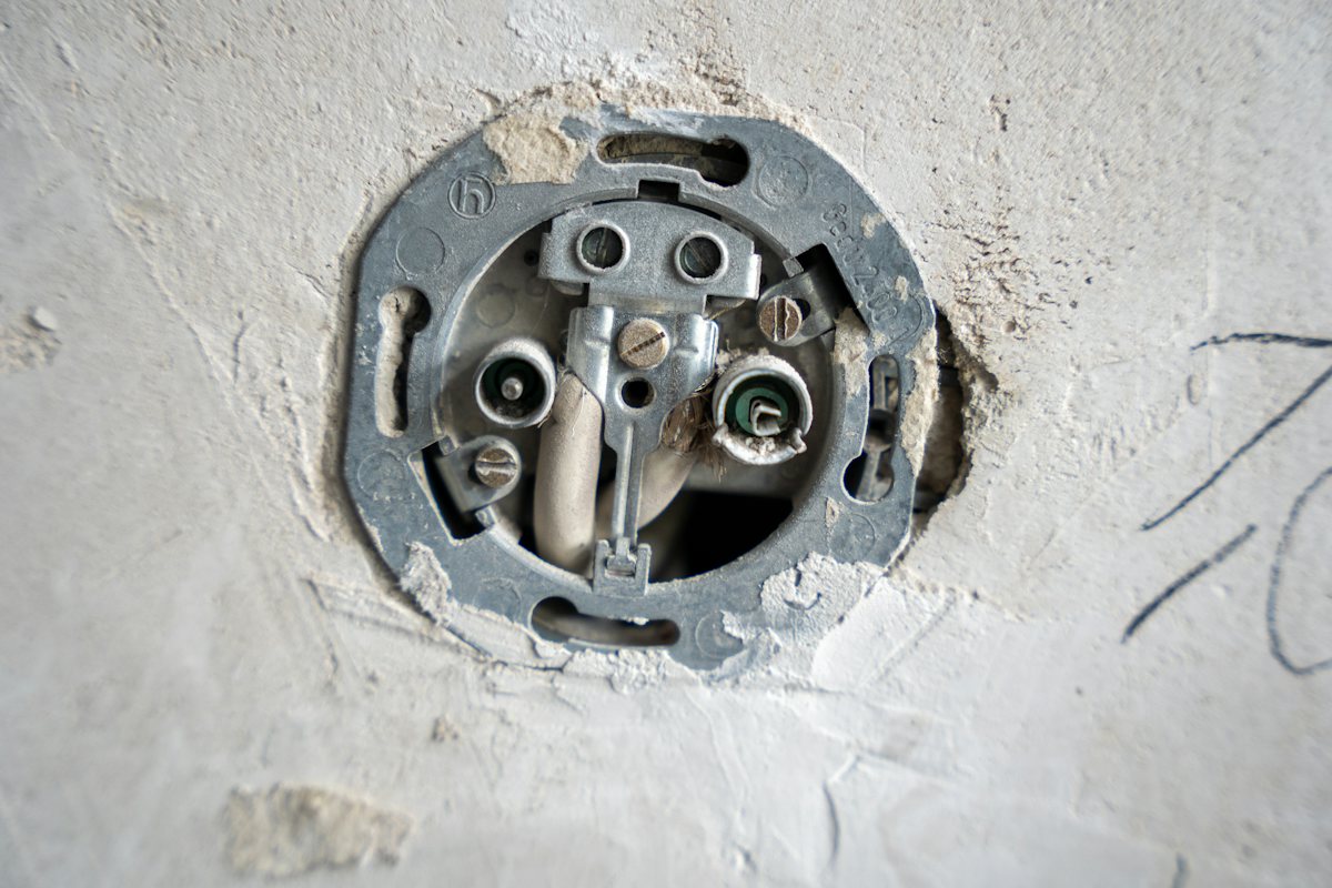 Wall outlet box opened up with its wires exposed in a plaster wall
