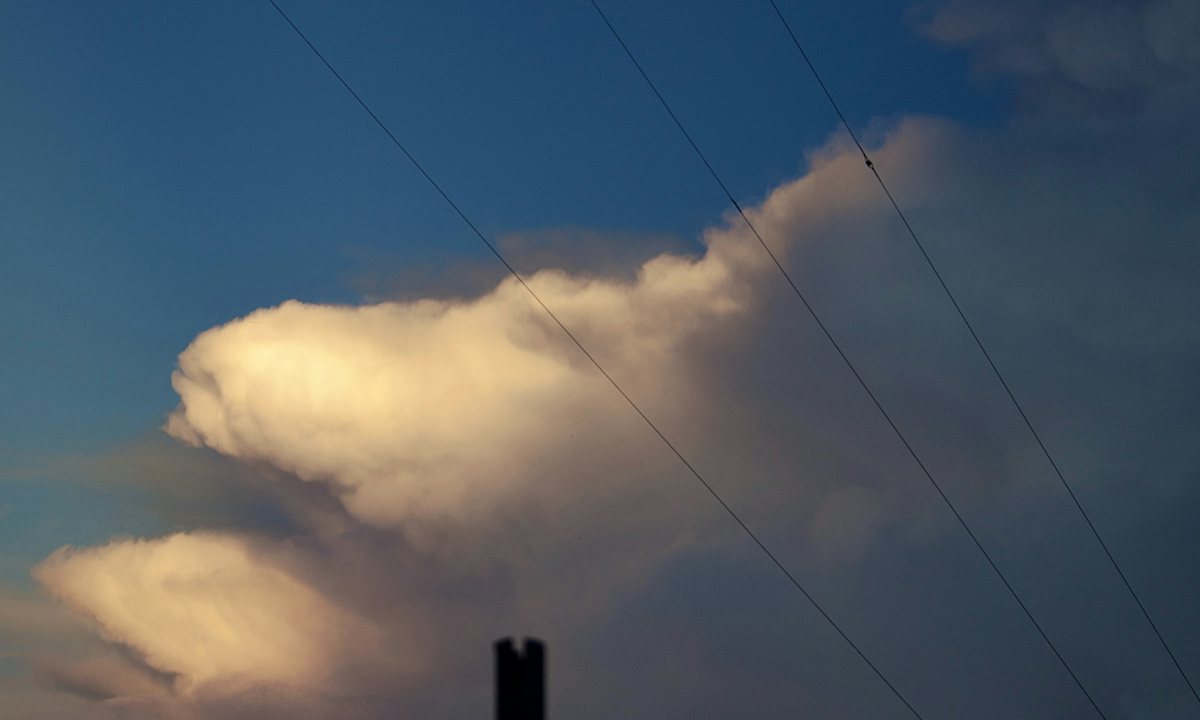 Overhead power lines crossing a blue sky under a large cloud